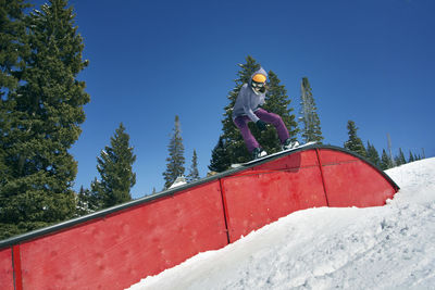 Woman snowboarding on railing on snow covered mountains against clear sky