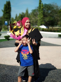 Boy gesturing peace sign standing against sister on sunny day