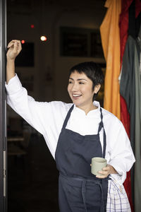 Smiling female chef with short hair standing at doorway of restaurant