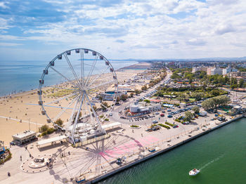 High angle view of ferris wheel by sea against sky
