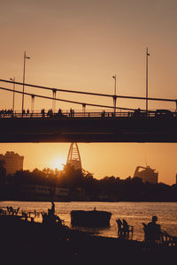 Silhouette people on bridge and beach against sky during sunset