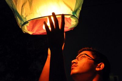 Close-up of teenage boy releasing lit paper lantern at night