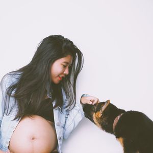 Smiling pregnant woman playing with dog against white background