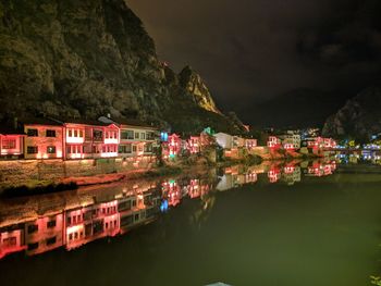 Buildings by lake against sky at night