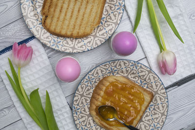 Colored easter egg in plate on a breakfast table with jam and pink white tulips.