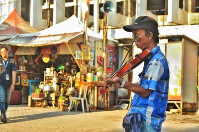 Side view of mature man playing violin while standing on city street