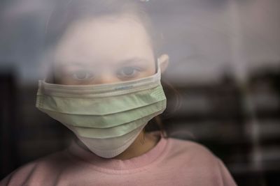 Close-up portrait of girl wearing mask looking through window