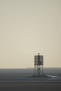 Cross on stilt at beach against clear sky during foggy weather