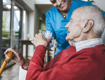 Smiling nurse giving water to senior man at home