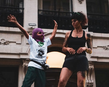 Full length of woman with arms raised in front of building