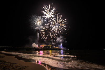 Firework display over sea against sky at night