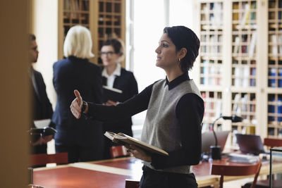 Side view of lawyer researching while colleagues standing in background at library