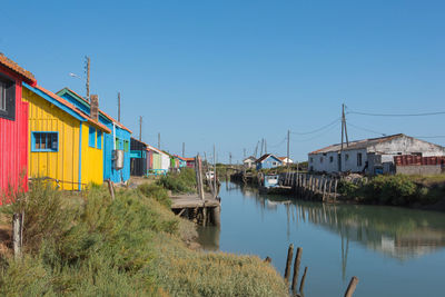 Houses by river and buildings against clear blue sky