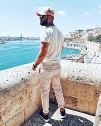 Man standing on retaining wall by sea against cityscape