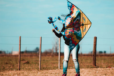 Woman with kite standing on field against blue sky