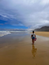 Rear view of woman walking at beach against sky