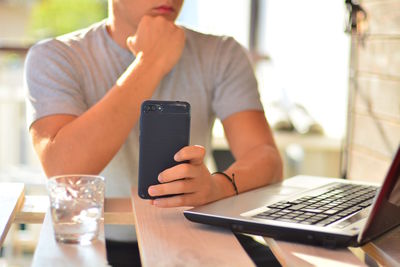 Midsection of man using technologies at table in cafe