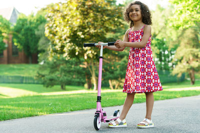 Full length of smiling woman with push scooter at park