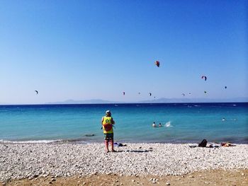 Rear view of man standing at beach against sky