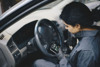 Female mechanic using mobile phone while sitting in car