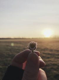 Close-up of hand holding sunglasses against sky during sunset