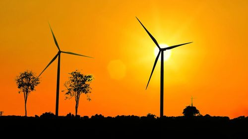 Silhouette of wind turbines on field against sky during sunset