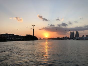 Silhouette buildings by sea against sky during sunset