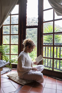 Side view of woman sitting on window