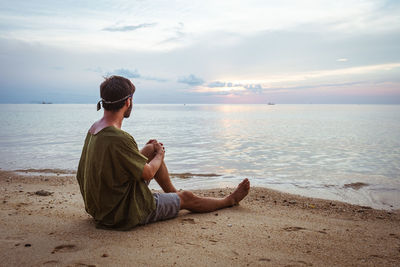 Young man looking at sea against sky during sunset