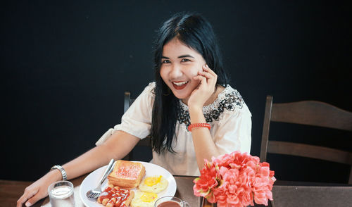 Portrait of smiling woman with breakfast on table sitting against black background