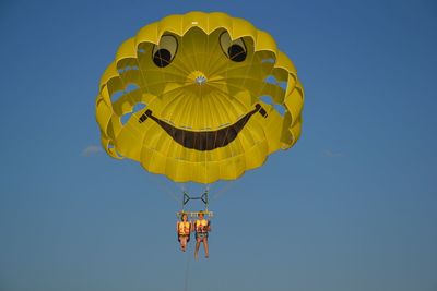 Full length portrait of smiling couple parasailing against sky