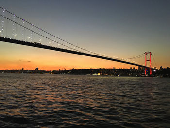 Silhouette bridge over river against sky during sunset