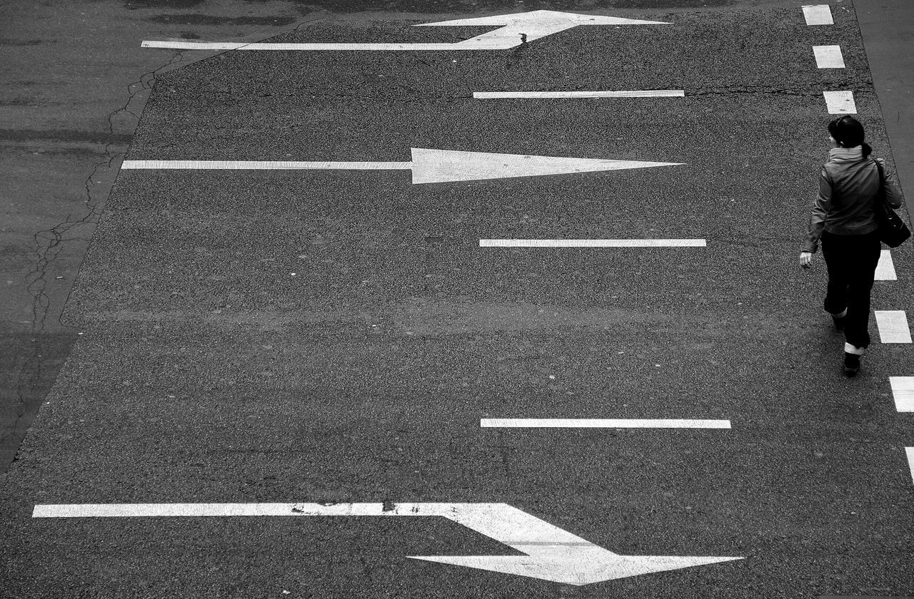 road marking, street, road, zebra crossing, asphalt, high angle view, men, walking, lifestyles, transportation, standing, guidance, shadow, arrow symbol, leisure activity, day, sidewalk, outdoors