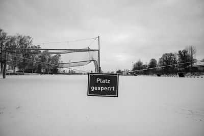 Road sign on snow covered field against sky