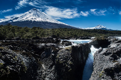 Scenic view of waterfall against snowcapped mountains