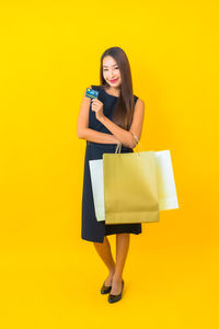 Portrait of young woman using phone against yellow background