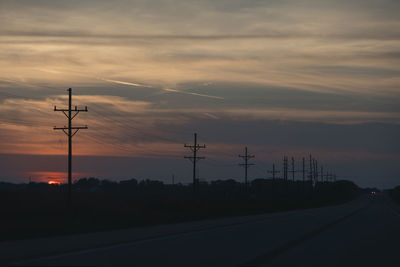 Silhouette electricity pylon by road against sky during sunset