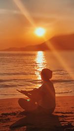 Rear view of woman sitting on beach during sunset