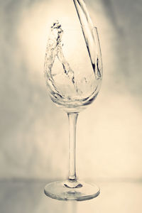 Water splashing in glass on table against wall