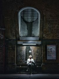 Full length of man sitting against wall in building