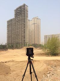 Camera with tripod on field against buildings during sunny day