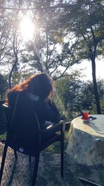 Woman sitting on chair against trees