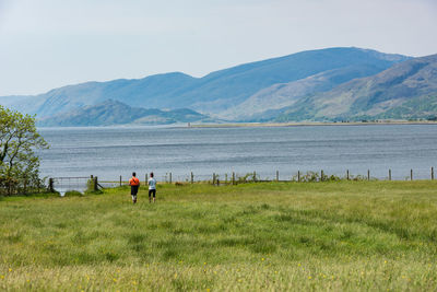 A couple of tourists approaching shore of loch linnhe through the green meadow, scotland, uk, europe