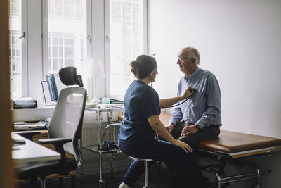 Female healthcare worker examining senior patient sitting on bed in clinic