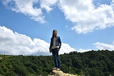 Full length of young woman standing on mountain peak against cloudy sky