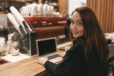 Adult confident serious smiling business woman freelancer working in a cafe using a laptop and phone