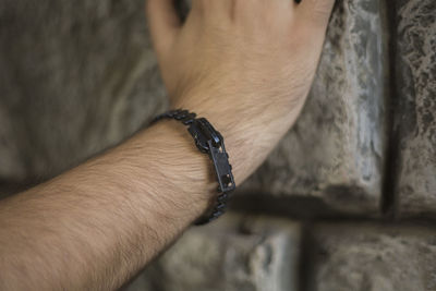 Close-up of hand wearing bracelet by wall