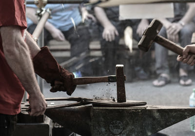 Midsection of blacksmith hammering on metal in workshop