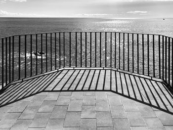 Shadow of railing on footpath by sea against sky