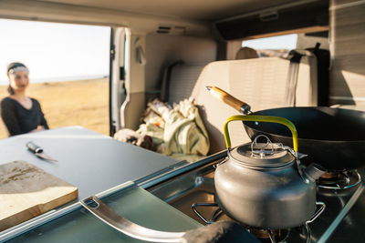 Close-up of teapot on stove with woman in background seen through camper van